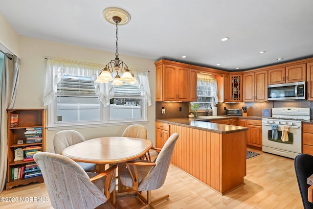 kitchen with light wood finished floors, a peninsula, white range with gas stovetop, a sink, and stainless steel microwave