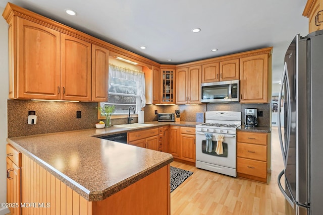 kitchen featuring light wood finished floors, a peninsula, a sink, decorative backsplash, and appliances with stainless steel finishes