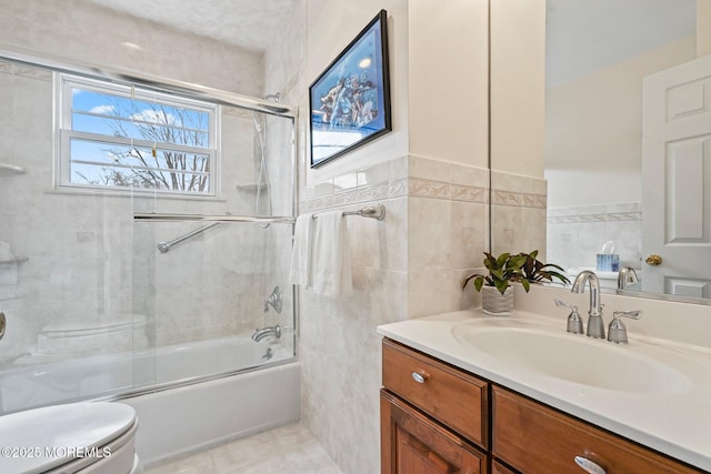 bathroom featuring vanity, shower / bath combination with glass door, tile patterned flooring, tile walls, and toilet