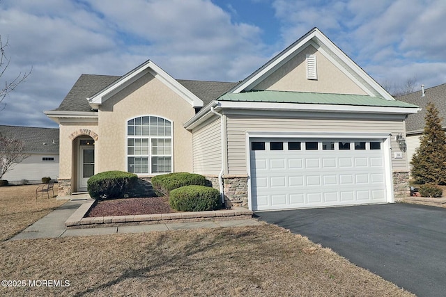 ranch-style house with driveway, a garage, stone siding, metal roof, and stucco siding