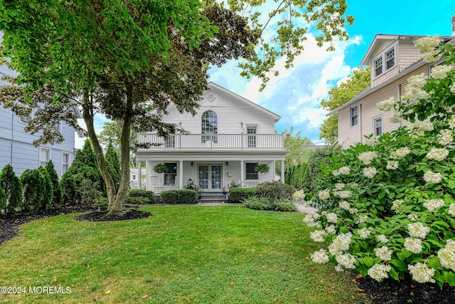 view of front of house featuring french doors, a balcony, and a front lawn