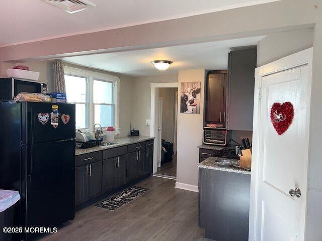 kitchen with dark wood-style floors, stainless steel microwave, visible vents, freestanding refrigerator, and a sink