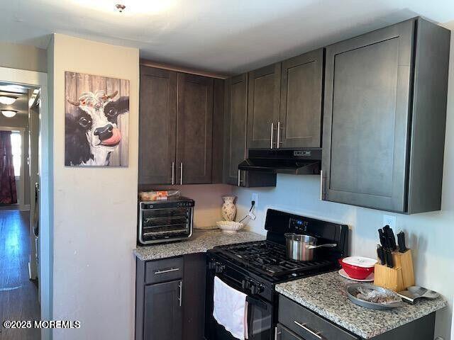 kitchen featuring dark brown cabinetry, black range with gas cooktop, a toaster, light stone counters, and under cabinet range hood