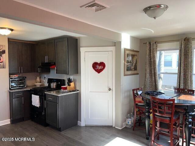 kitchen featuring a toaster, visible vents, wood finished floors, black gas stove, and under cabinet range hood