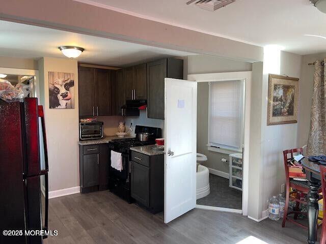 kitchen featuring black appliances, wood finished floors, visible vents, and under cabinet range hood