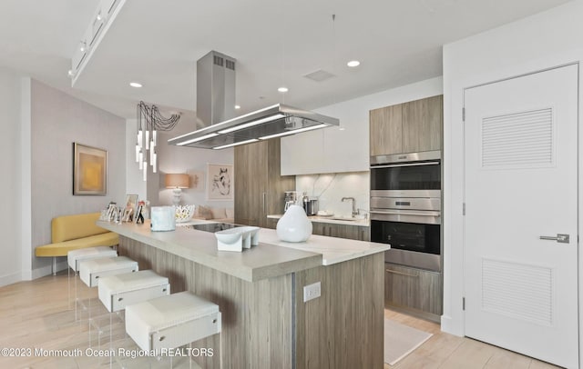 kitchen with a breakfast bar, island exhaust hood, double oven, a sink, and modern cabinets