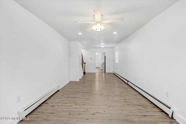 empty room with light wood finished floors, stairway, baseboard heating, and a ceiling fan