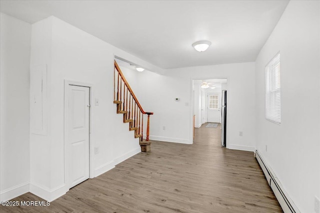 empty room with ceiling fan, wood finished floors, baseboards, stairway, and baseboard heating