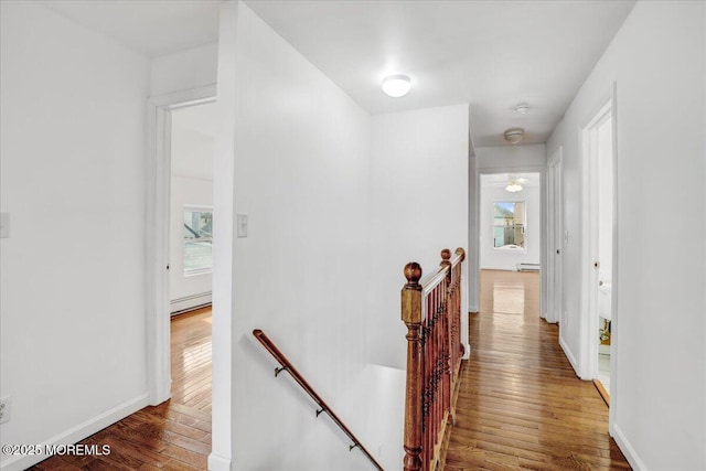 hallway with baseboard heating, baseboards, an upstairs landing, and wood finished floors