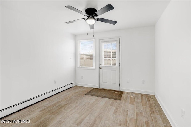 spare room featuring light wood finished floors, a baseboard radiator, baseboards, and a ceiling fan