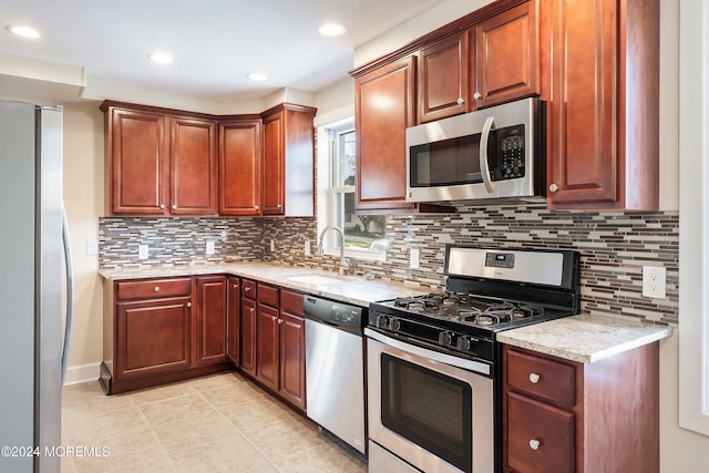 kitchen with light stone counters, backsplash, appliances with stainless steel finishes, light tile patterned flooring, and a sink