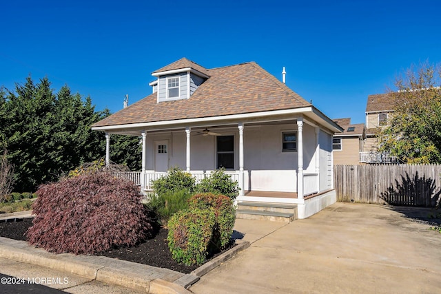 bungalow-style home with covered porch, ceiling fan, fence, and roof with shingles