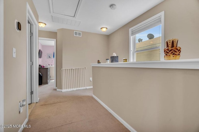 hallway with attic access, visible vents, light carpet, and baseboards