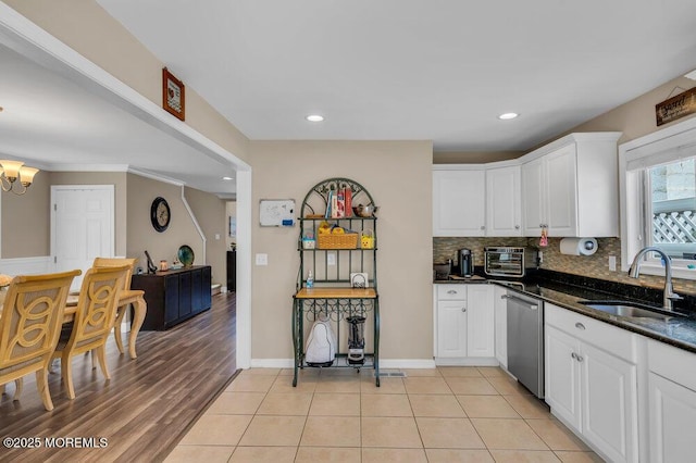 kitchen with light tile patterned floors, tasteful backsplash, a sink, white cabinetry, and stainless steel dishwasher