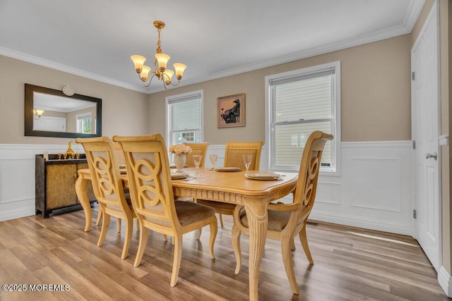 dining room with ornamental molding, a wainscoted wall, a notable chandelier, and light wood finished floors