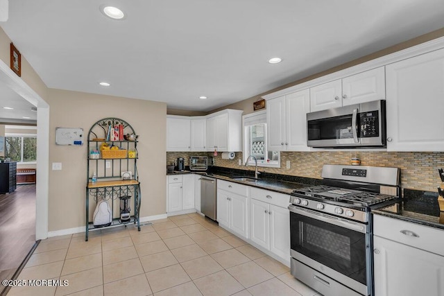 kitchen with light tile patterned flooring, a sink, white cabinetry, appliances with stainless steel finishes, and backsplash