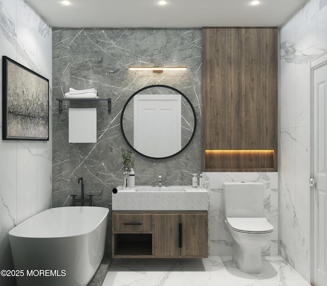 full bath featuring marble finish floor, a freestanding tub, vanity, and stone wall