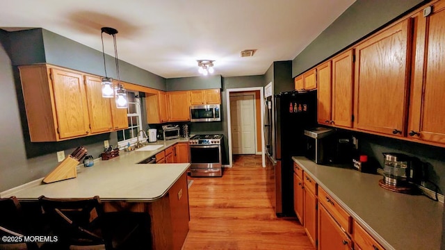 kitchen with light wood-style floors, a peninsula, appliances with stainless steel finishes, light countertops, and a sink