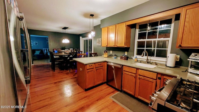 kitchen featuring light wood-style flooring, a peninsula, a sink, light countertops, and stainless steel appliances