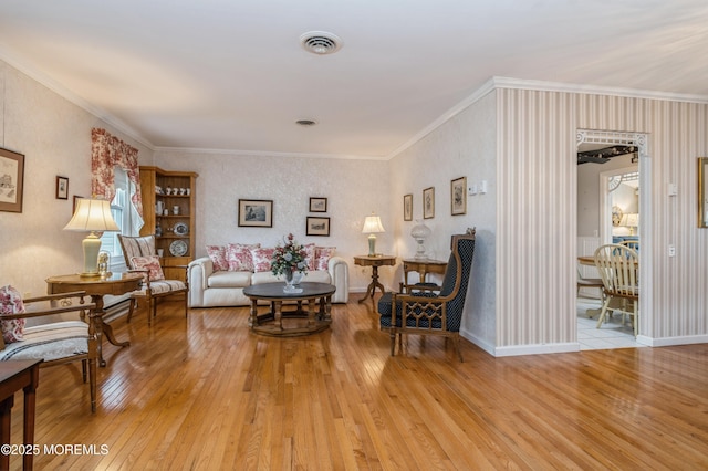 living room with ornamental molding, light wood-type flooring, visible vents, and baseboards