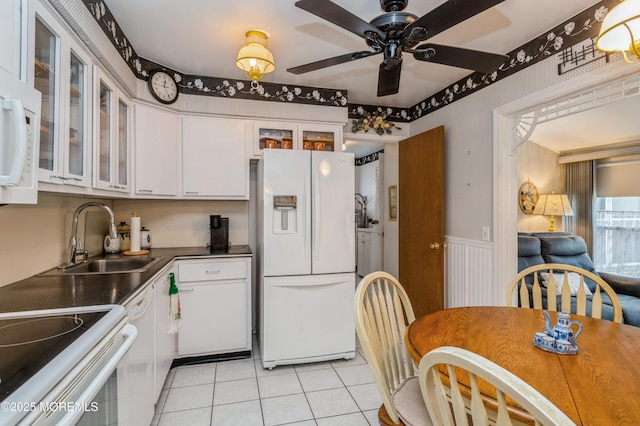 kitchen with white appliances, wainscoting, dark countertops, white cabinetry, and a sink