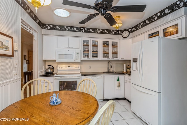 kitchen featuring white appliances, wallpapered walls, white cabinets, wainscoting, and a sink