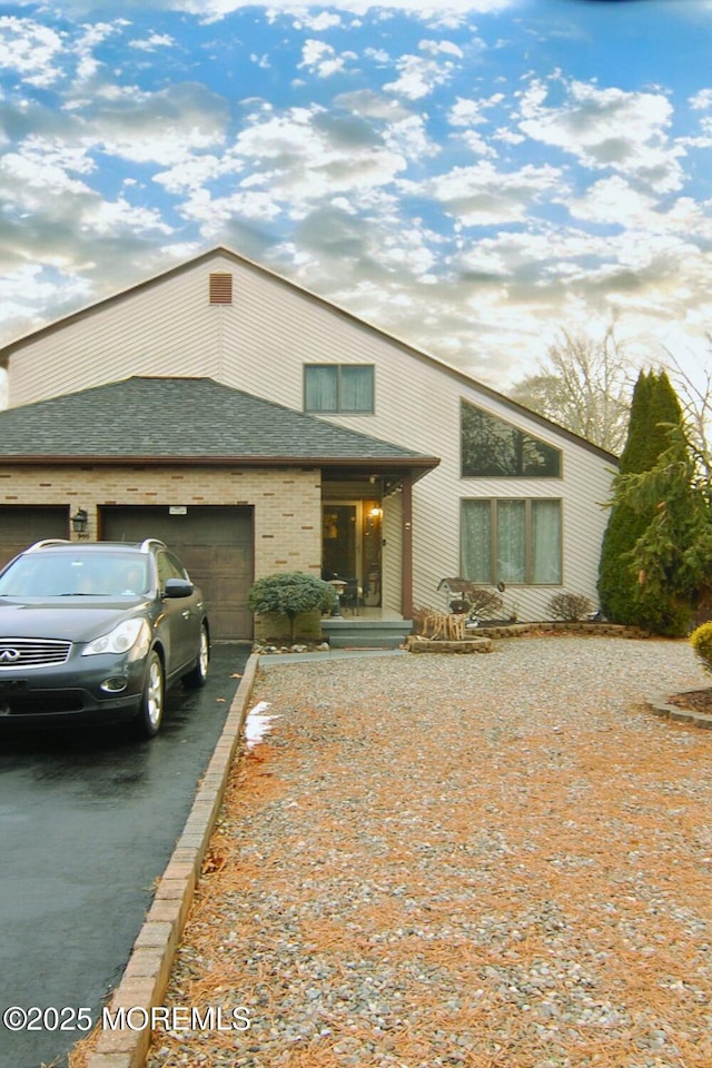 mid-century modern home with a garage, driveway, and roof with shingles