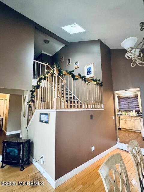 stairs with a chandelier, vaulted ceiling with skylight, wood finished floors, and baseboards