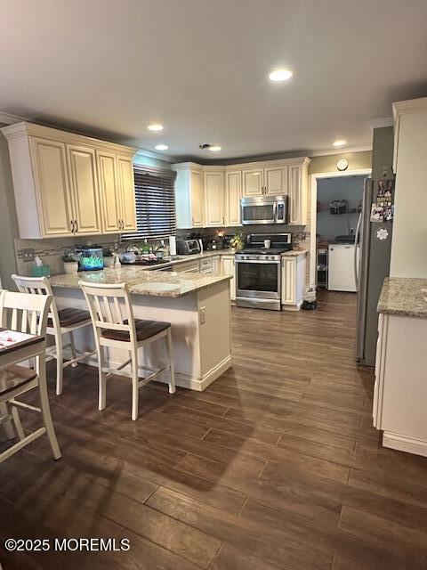 kitchen featuring light stone counters, a peninsula, dark wood-style flooring, appliances with stainless steel finishes, and decorative backsplash