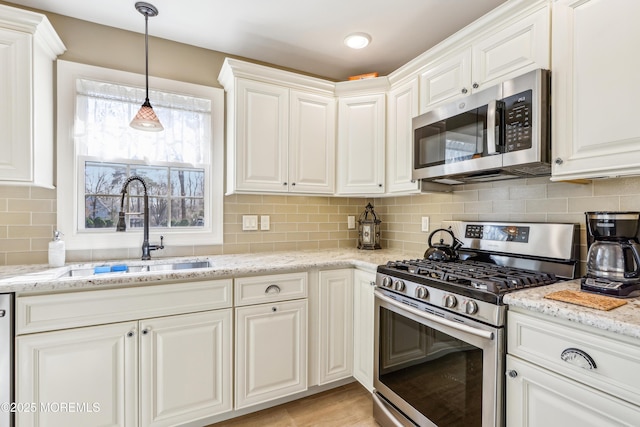 kitchen featuring light stone countertops, decorative backsplash, stainless steel appliances, white cabinetry, and a sink