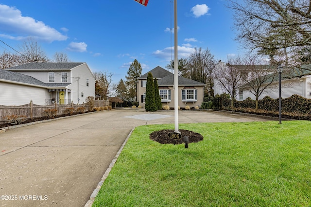 view of front of house with concrete driveway, fence, and a front lawn