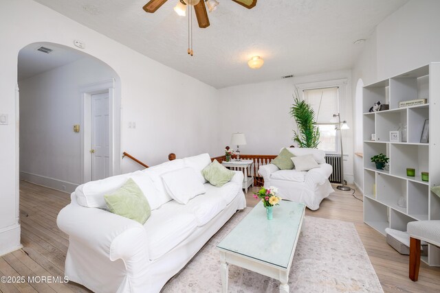 75 Highland Ave, Highlands, NJ 07732 - living area with visible vents, radiator heating unit, light wood-style flooring, arched walkways, and a ceiling fan