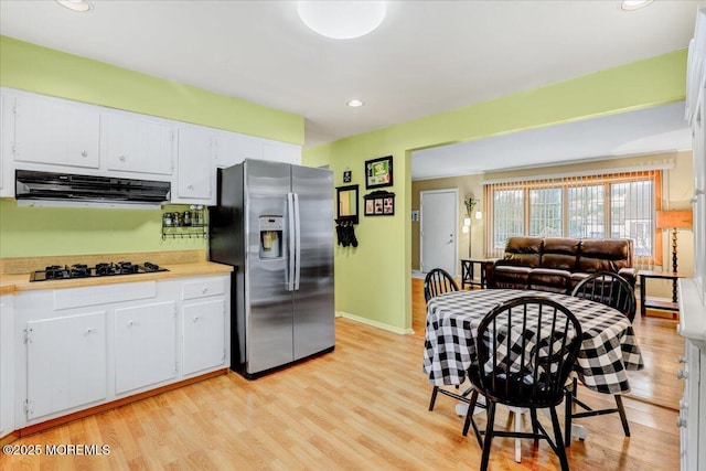 kitchen featuring light countertops, black gas stovetop, stainless steel refrigerator with ice dispenser, and range hood