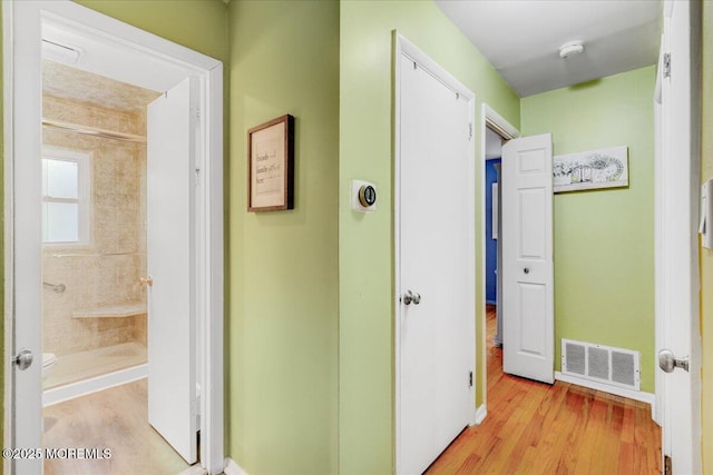 hall featuring baseboards, visible vents, and light wood finished floors