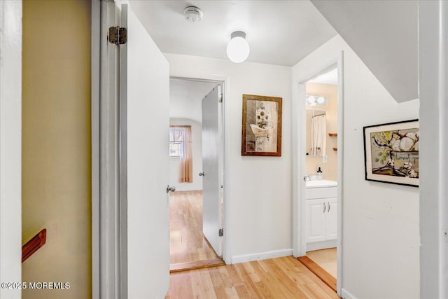 hallway with a sink, light wood-style flooring, and baseboards