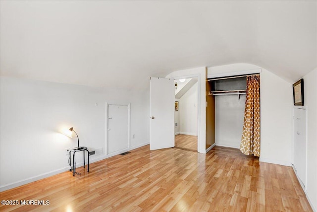 unfurnished bedroom with lofted ceiling, light wood finished floors, a closet, and baseboards