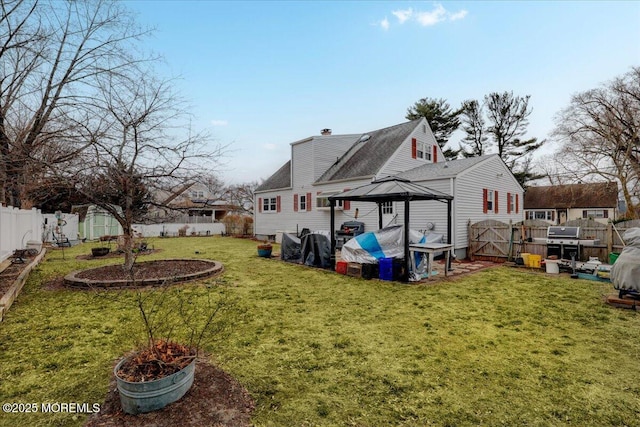 back of property with a fenced backyard, a chimney, a lawn, and a gazebo