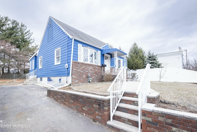 bungalow featuring a shingled roof, brick siding, and fence