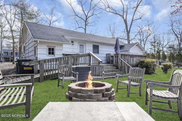 back of property featuring a yard, a fire pit, a deck, and a shingled roof