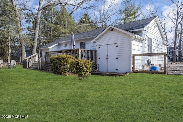 back of house featuring a wooden deck, an outbuilding, a lawn, and a shingled roof