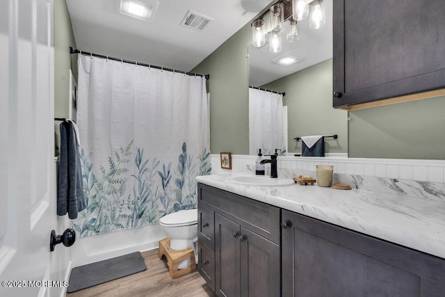 bathroom featuring vanity, wood finished floors, visible vents, shower / bath combo with shower curtain, and toilet