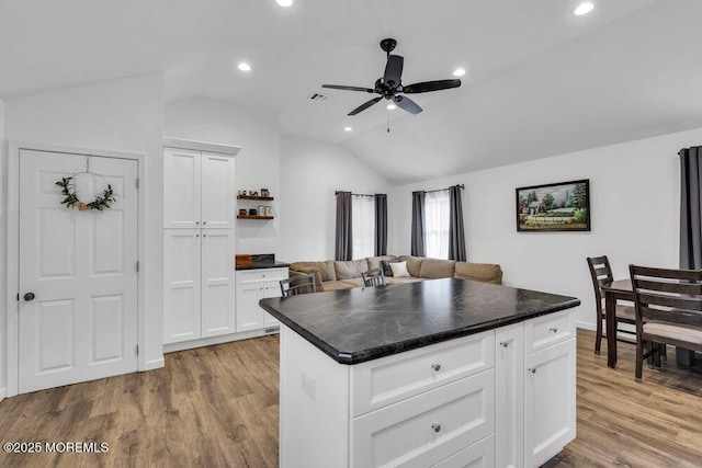 kitchen featuring vaulted ceiling, white cabinets, wood finished floors, and dark countertops