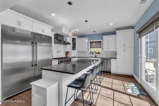 kitchen featuring a sink, appliances with stainless steel finishes, wall chimney exhaust hood, white cabinets, and dark wood-style flooring