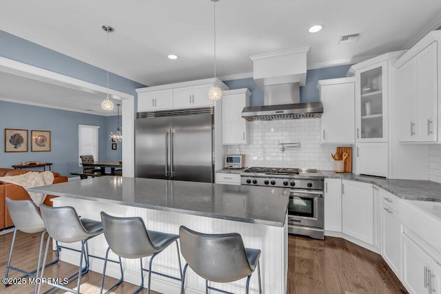 kitchen with glass insert cabinets, high quality appliances, ornamental molding, dark wood-style floors, and wall chimney exhaust hood