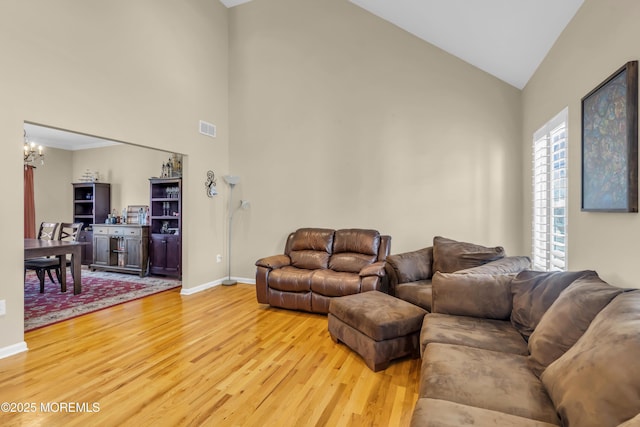 living room with high vaulted ceiling, visible vents, baseboards, light wood finished floors, and an inviting chandelier