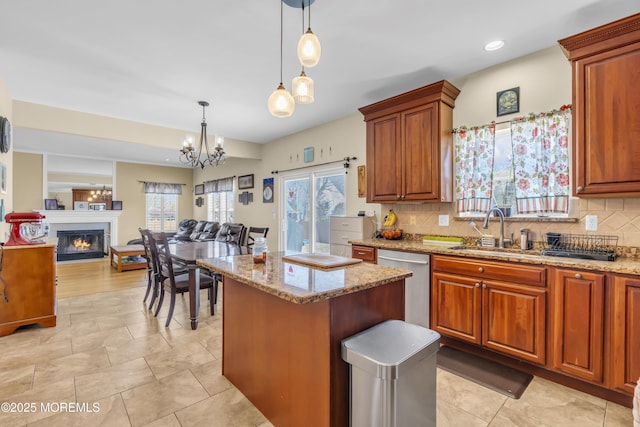 kitchen with a center island, tasteful backsplash, a glass covered fireplace, light stone countertops, and dishwasher