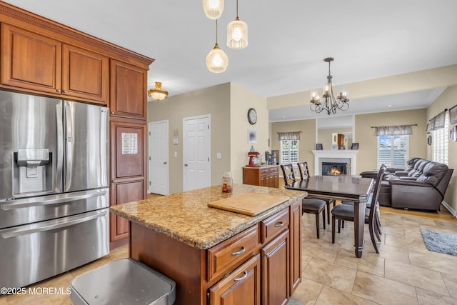 kitchen with a center island, brown cabinets, stainless steel refrigerator with ice dispenser, a glass covered fireplace, and light stone countertops