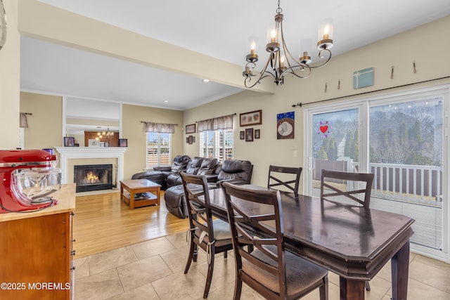 dining area featuring a chandelier, a glass covered fireplace, light tile patterned flooring, and crown molding