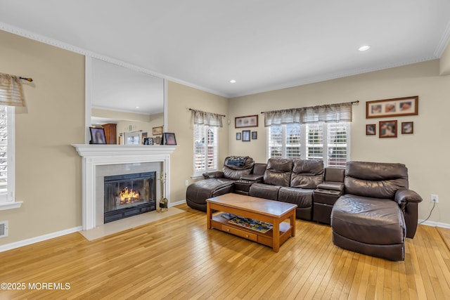 living room featuring light wood-type flooring, plenty of natural light, crown molding, and a fireplace with flush hearth