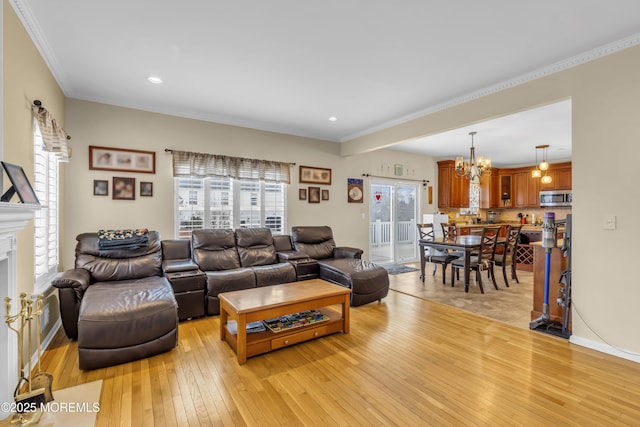 living room with a fireplace, a notable chandelier, light wood finished floors, ornamental molding, and baseboards